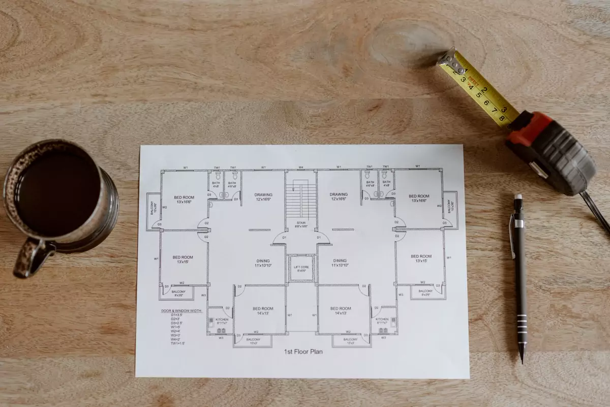 Grundriss, Maßband und Stift neben einer Tasse Kaffee auf einem Tisch